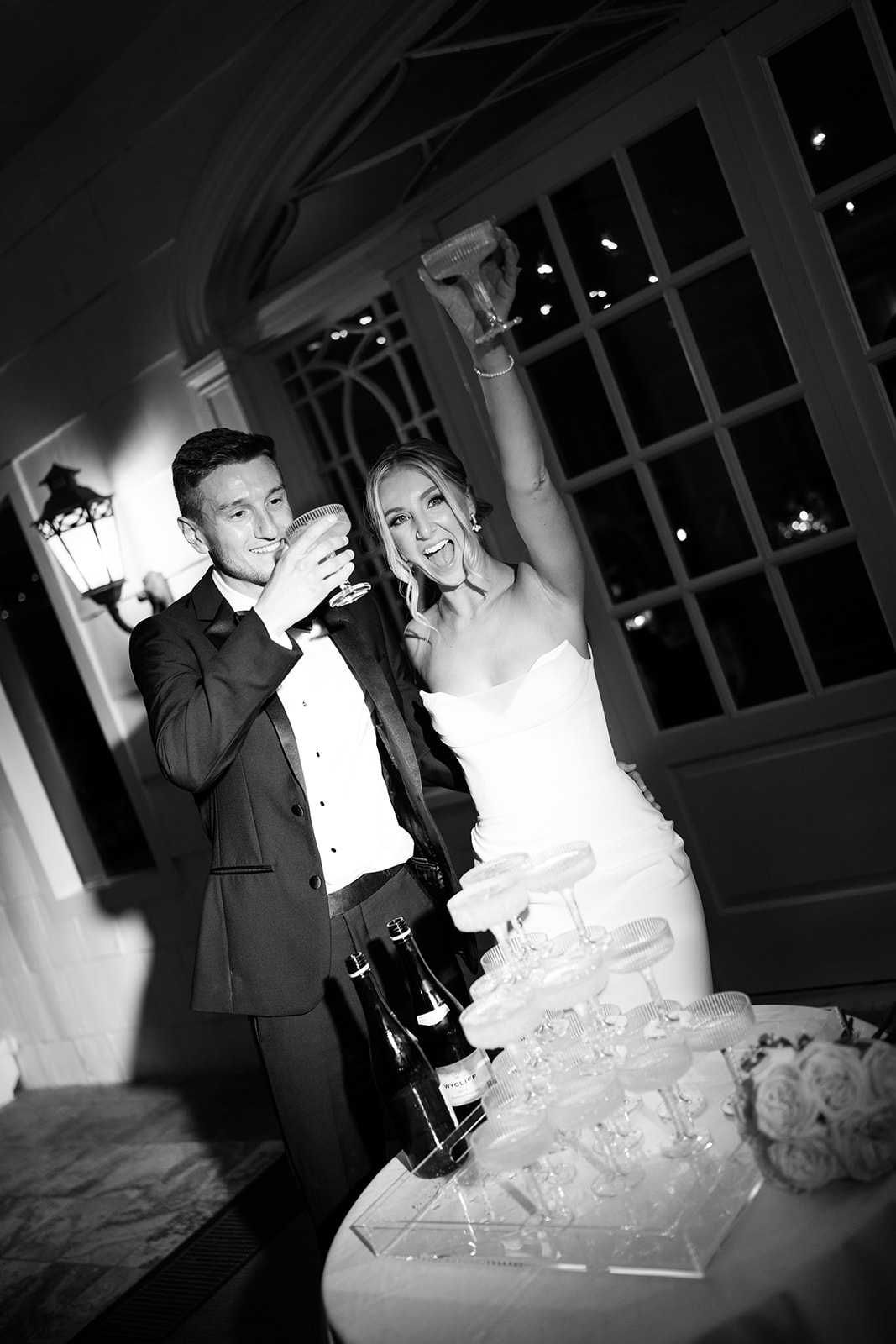 Black and white photo of the newlyweds raising their champagne glasses in a toast by their glass tower.
